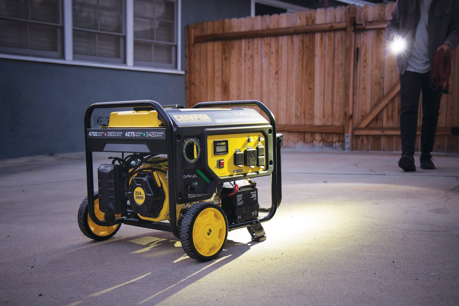 Champion dual fuel portable generator powering emergency home backup outside a house at night with extension cords and built-in outlet panel visible