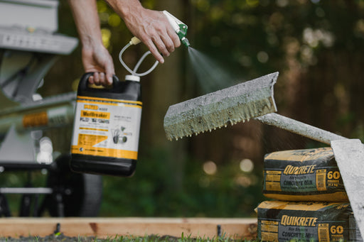 Spraying MudBreaker on a concrete-crusted tool next to bags of concrete mix
