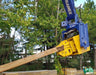 RAMEX auto-tilting vibro hammer gripping a steel pile at the edge of a wooded site
