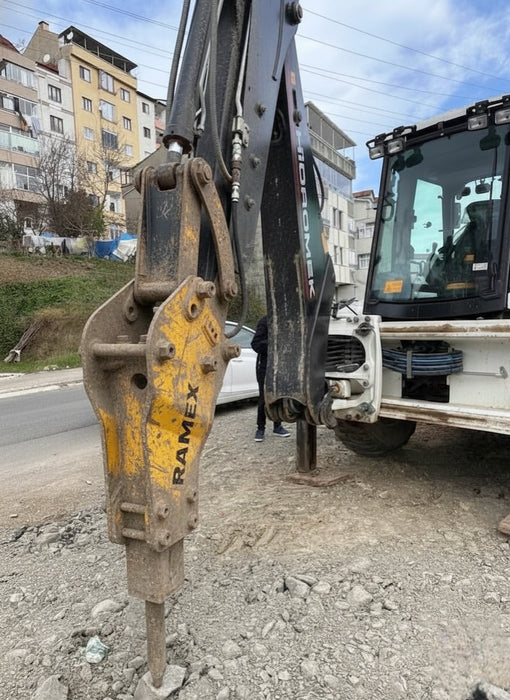 RAMEX RAM hydraulic breaker working beside an excavator cab on a street site, representative photo